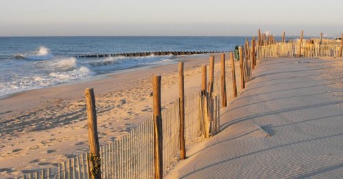 A sandy beach with wooden fences, gentle waves, and a calm ocean under a clear sky during sunset.