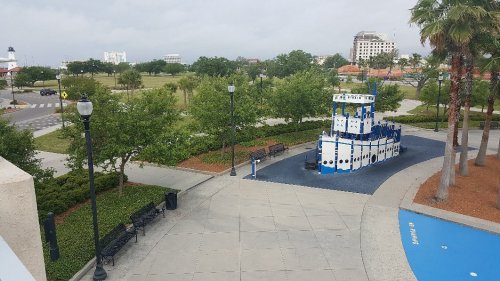 A park scene featuring a blue and white boat sculpture, benches, and trees under a cloudy sky.