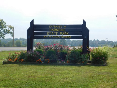 Sign for Harmonie State Park, featuring colorful flowers and greenery, with a road visible in the background.
