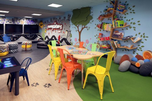 A colorful children's playroom with a table, chairs, bookshelves, and cozy seating areas.