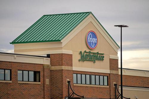 Signage of a Kroger Marketplace store with a green roof and brick exterior under a cloudy sky.