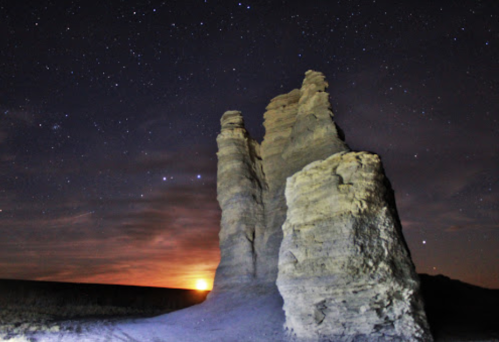 A rocky formation under a starry sky, with a glowing sunset on the horizon.