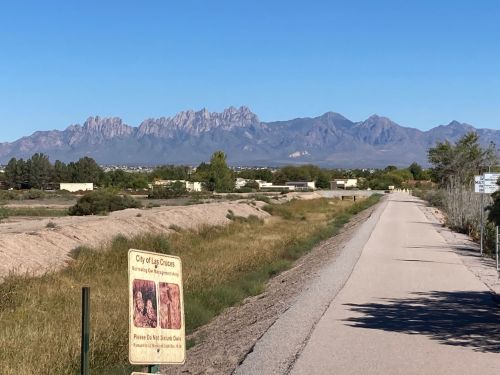 A scenic view of mountains in the distance, with a pathway and a sign for the City of Las Cruces in the foreground.