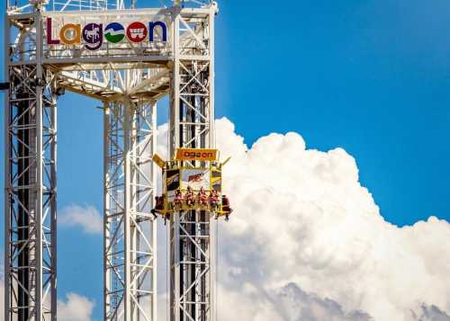 A group of people on a thrill ride at Lagoon amusement park, with a blue sky and fluffy clouds in the background.