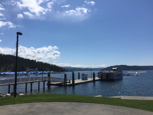 A serene lake view with a wooden dock, boats, and blue skies dotted with clouds, surrounded by green hills.