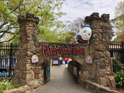 Entrance to Fairytale Town, featuring a stone archway and a colorful sign with a cartoon character peeking out.