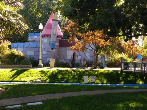 Colorful play castle surrounded by greenery and trees in a sunny park setting.
