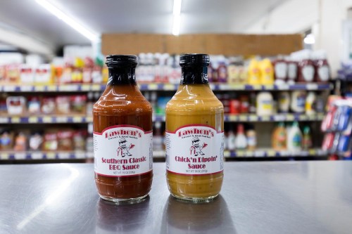 Two bottles of Lawhorn's BBQ sauces, Southern Classic BBQ and Chick'n Dippin', displayed on a counter with shelves in the background.
