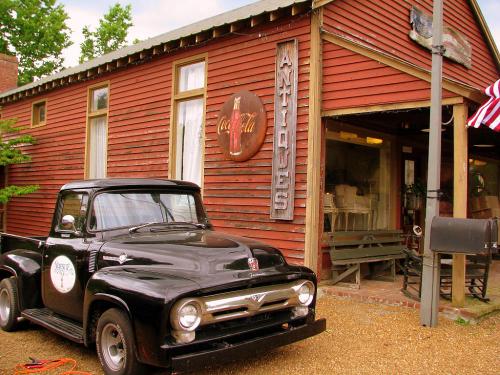 A vintage black truck parked in front of a red antique shop with a Coca-Cola sign and outdoor seating.