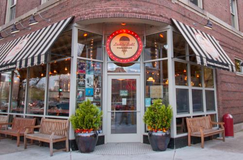 A cozy ice cream shop with striped awnings, bright signage, and outdoor seating on a brick building corner.