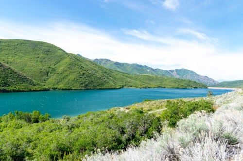 A serene landscape featuring a turquoise lake surrounded by lush green hills under a clear blue sky.