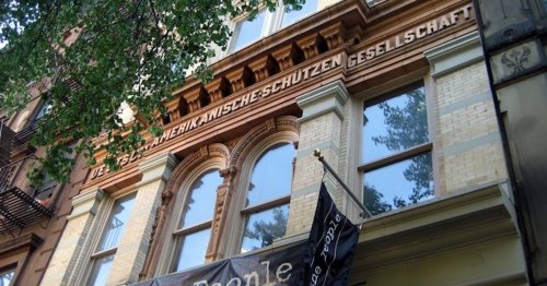 Historic building facade featuring ornate brickwork and large windows, with German text above the entrance.