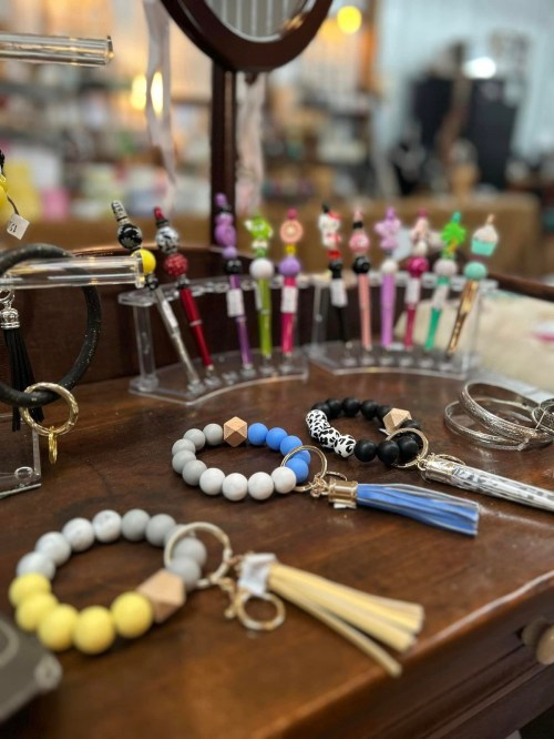 Colorful pens and keychains displayed on a wooden table, featuring beads and tassels in various styles.