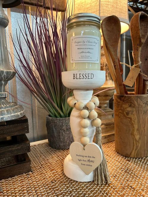 A decorative candle holder with a jar candle, wooden beads, and a "Blessed" sign, set against a cozy background.