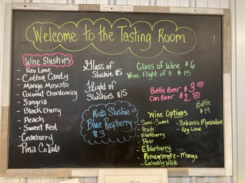 Chalkboard menu for a tasting room featuring wine slushies, wine options, and prices for drinks.
