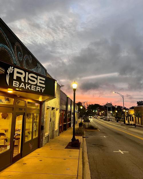 A bakery storefront at dawn, with a street lamp and colorful clouds in the sky.