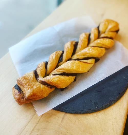 A twisted pastry with a golden-brown crust and chocolate filling, resting on a piece of parchment paper.