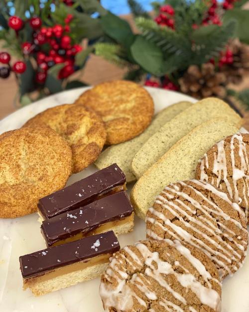 A platter of assorted cookies, including snickerdoodles, shortbread, and caramel bars, with festive greenery in the background.