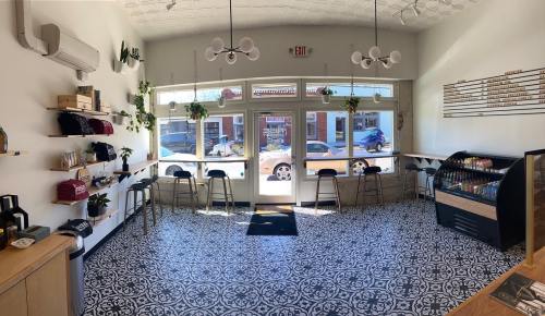 Bright café interior with patterned floor, shelves displaying merchandise, and large windows letting in natural light.