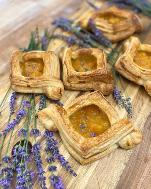 Five golden pastries with a fruit filling, arranged on a wooden surface adorned with sprigs of lavender.