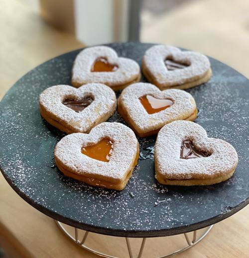 A platter of heart-shaped cookies filled with jam and chocolate, dusted with powdered sugar.