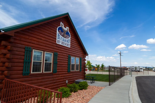 A log cabin-style building with a sign for Buckhorn RV Resort, surrounded by a gravel path and open sky.