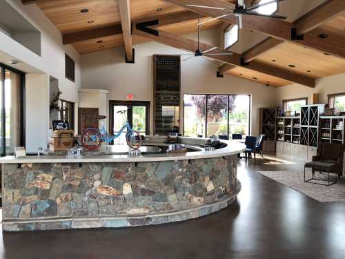 A modern interior featuring a stone bar, wooden beams, large windows, and a cozy seating area with bookshelves.