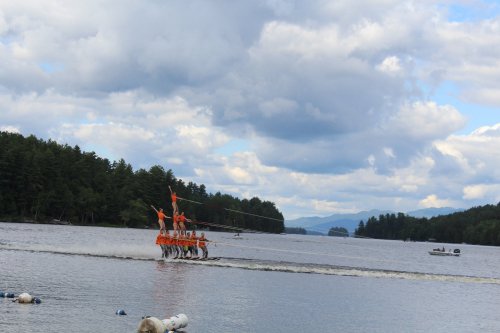A group of people in orange shirts walking on water, with trees and clouds in the background.