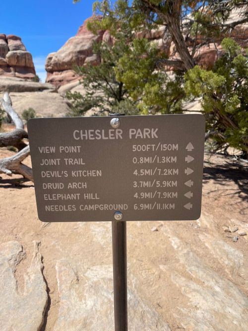 Signpost at Chesler Park showing trail distances to various landmarks and viewpoints in a desert landscape.