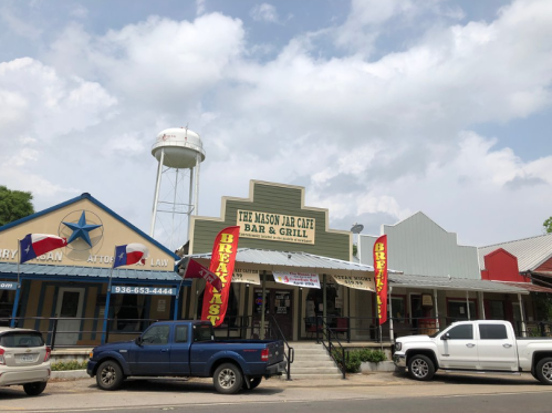 A small town street featuring The Mason Jar Cafe Bar & Grill, with a water tower and nearby buildings.