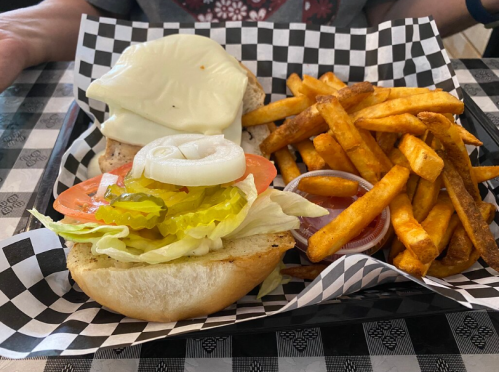 A sandwich with lettuce, tomato, pickles, and mozzarella cheese, served with a side of golden fries on a checkered tray.