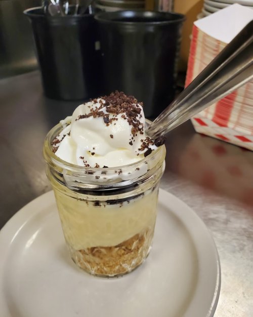 A dessert in a jar with layers of cream, crushed cookies, and topped with whipped cream and chocolate crumbs.
