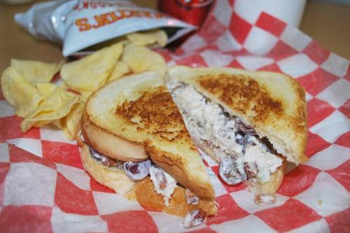 A toasted sandwich filled with chicken salad, served with potato chips on a red and white checkered paper.