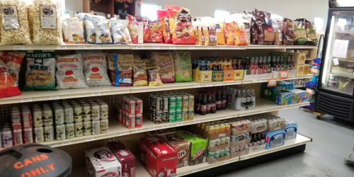 A grocery store shelf filled with various snacks, drinks, and packaged foods, including chips and soda.