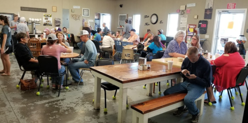 A busy community gathering space with people seated at tables, chatting and enjoying each other's company.