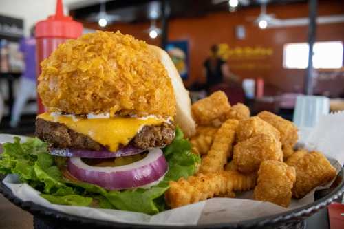 A close-up of a burger topped with a crispy onion ring, lettuce, and cheese, served with crinkle-cut fries on the side.