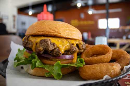 A juicy cheeseburger with lettuce, tomato, and onion, served with crispy onion rings on the side.