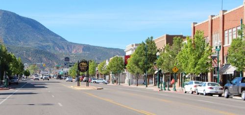 A wide street lined with trees and shops, with a mountain backdrop under a clear blue sky.