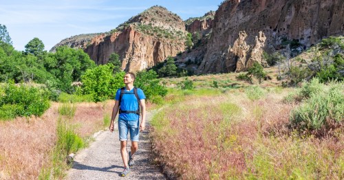 Main Loop path trail with man walking in Bandelier National Monument in New Mexico in Los Alamos with canyon cliffs.