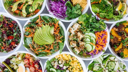 A colorful assortment of fresh salads in bowls, featuring greens, vegetables, and toppings like avocado and tofu.
