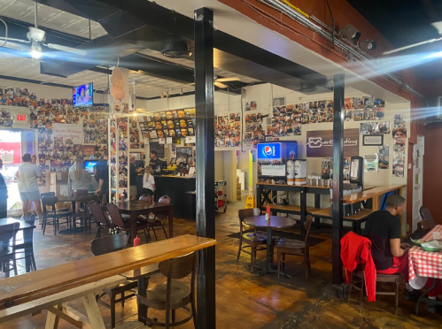 A cozy restaurant interior with a collage of photos on the walls, tables, and a counter with staff serving customers.