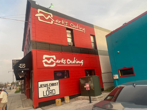 A red and black building with "Mark's Outing" sign and a "Jesus Christ is Lord" message on the wall.