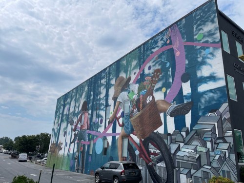 A vibrant mural depicting two children riding a bicycle through a colorful forest, with a basket full of flowers.