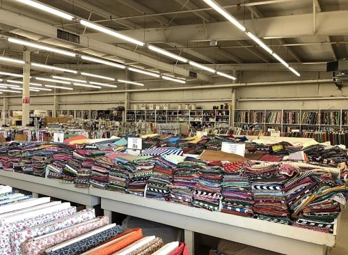 A spacious fabric store with colorful stacks of fabric on tables and shelves filled with various patterns and textures.