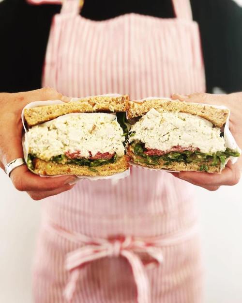 A person holding a sandwich cut in half, revealing layers of chicken salad, lettuce, and whole grain bread.