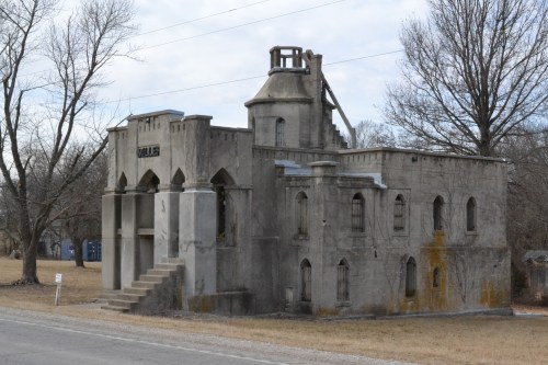 A weathered, abandoned building with gothic architecture, featuring arched windows and a partially collapsed roof.