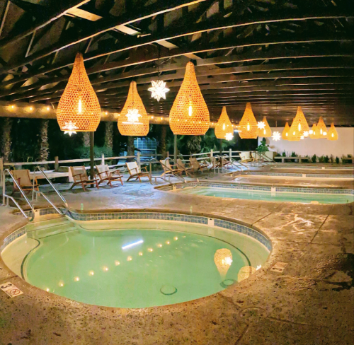 A serene spa area with hot tubs, surrounded by hanging lights and a wooden ceiling, creating a relaxing atmosphere.