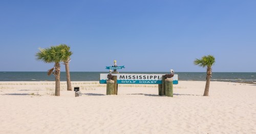 a large sign that says welcome to mississippi gulf coast in front of a sandy beach and water in the background