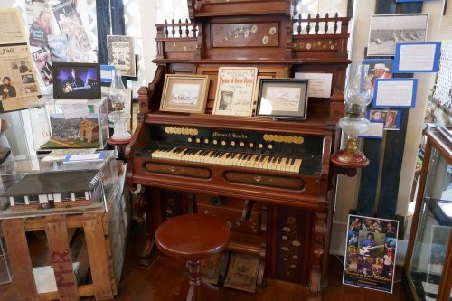 A vintage organ displayed in a museum, surrounded by historical artifacts and framed photographs.