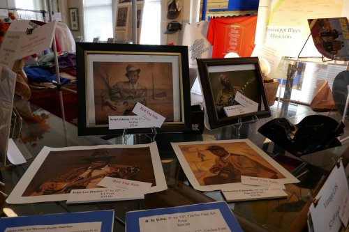 A display of framed artwork featuring musicians, with price tags and various items in the background.